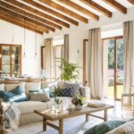 Salón comedor con vigas de madera vistas, sofá claro y puertas acristaladas al jardín
