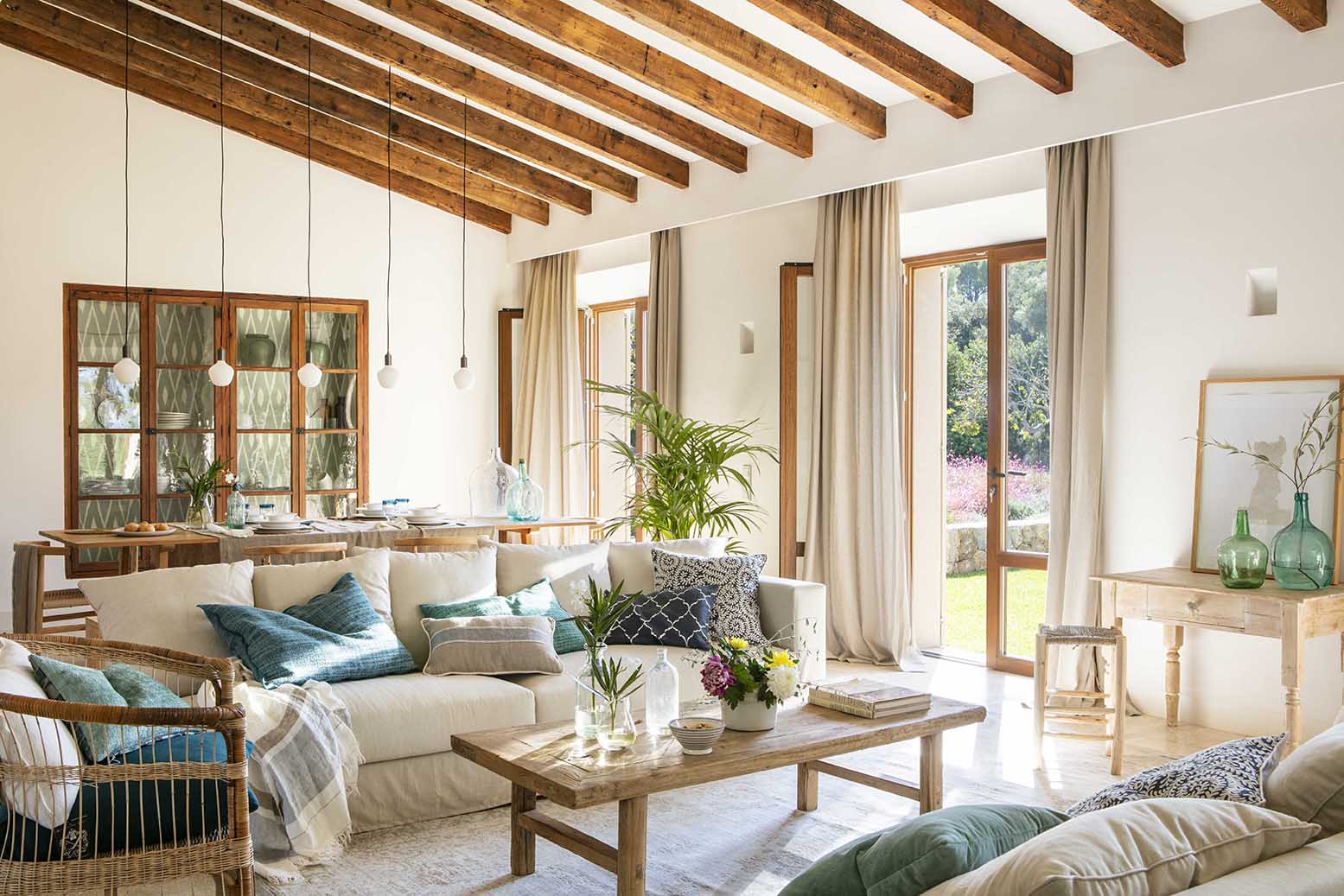 Salón comedor con vigas de madera vistas, sofá claro y puertas acristaladas al jardín