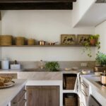 Cocina con fregadero de piedra, grifo dorado, estante abierto con cestas y suelo de baldosas de barro