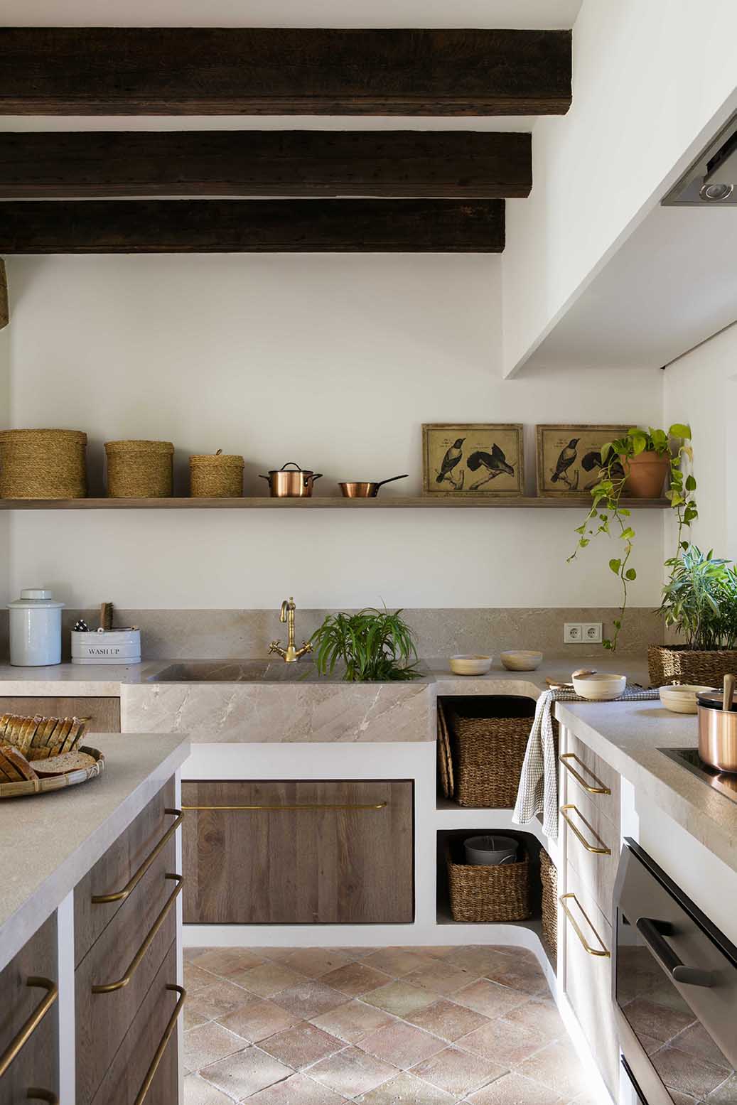 Cocina con fregadero de piedra, grifo dorado, estante abierto con cestas y suelo de baldosas de barro