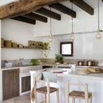 Barra de la cocina con dos taburetes de madera, gran viga antigua, fregadero de piedra y ventana pequeña