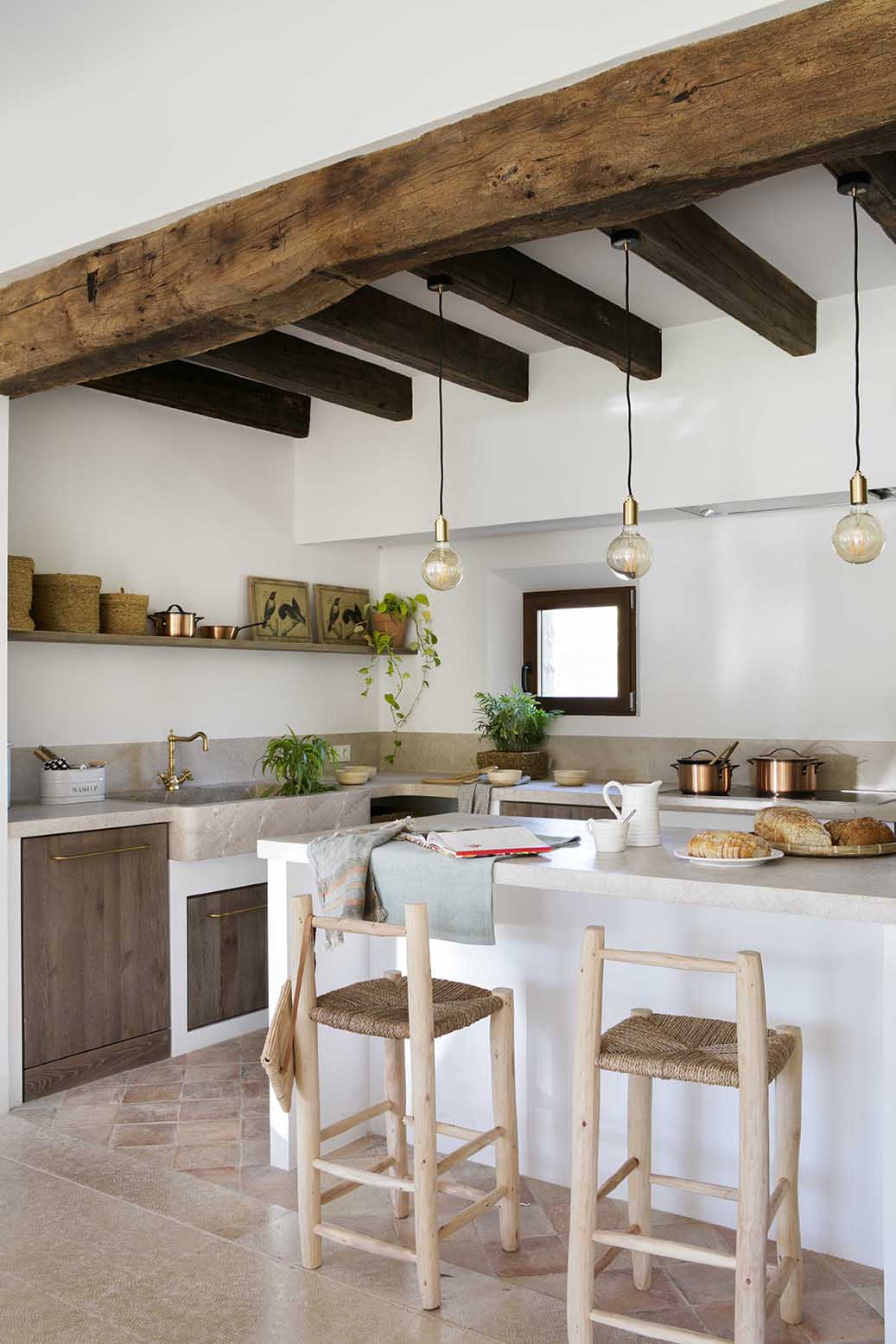 Barra de la cocina con dos taburetes de madera, gran viga antigua, fregadero de piedra y ventana pequeña