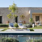 Piscina rodeada de lavanda frente a la casa de piedra, con porche y comedor exterior