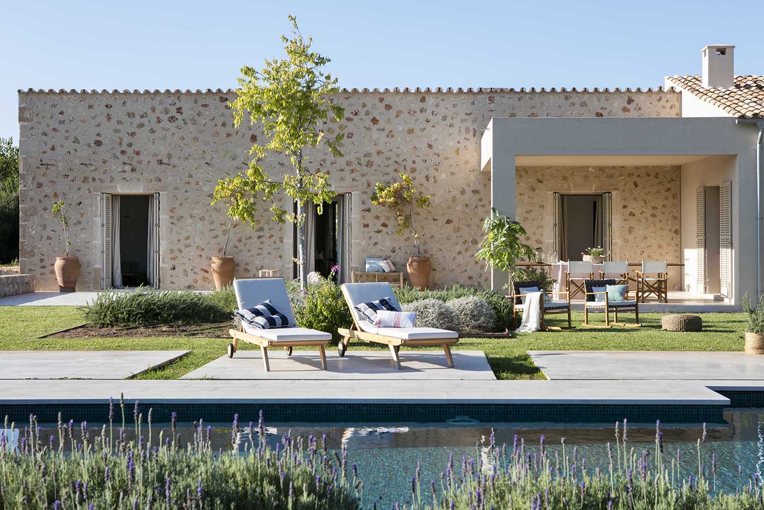 Piscina rodeada de lavanda frente a la casa de piedra, con porche y comedor exterior