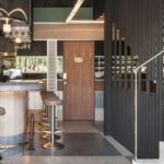 Bar counter with stools, a wooden door and black lattice screen beside a pale stone staircase