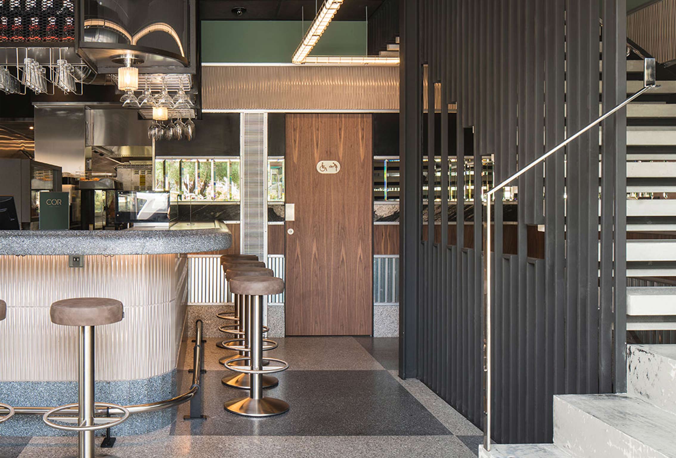 Bar counter with stools, a wooden door and black lattice screen beside a pale stone staircase