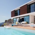 Terrasse mit Holzdeck, Sonnenliegen und Pool vor der Fassade aus Holzlamellen und Glas