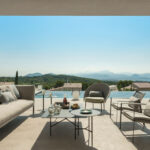 Beige sofa and braided rope armchairs under the porch, with an infinity pool and mountains behind