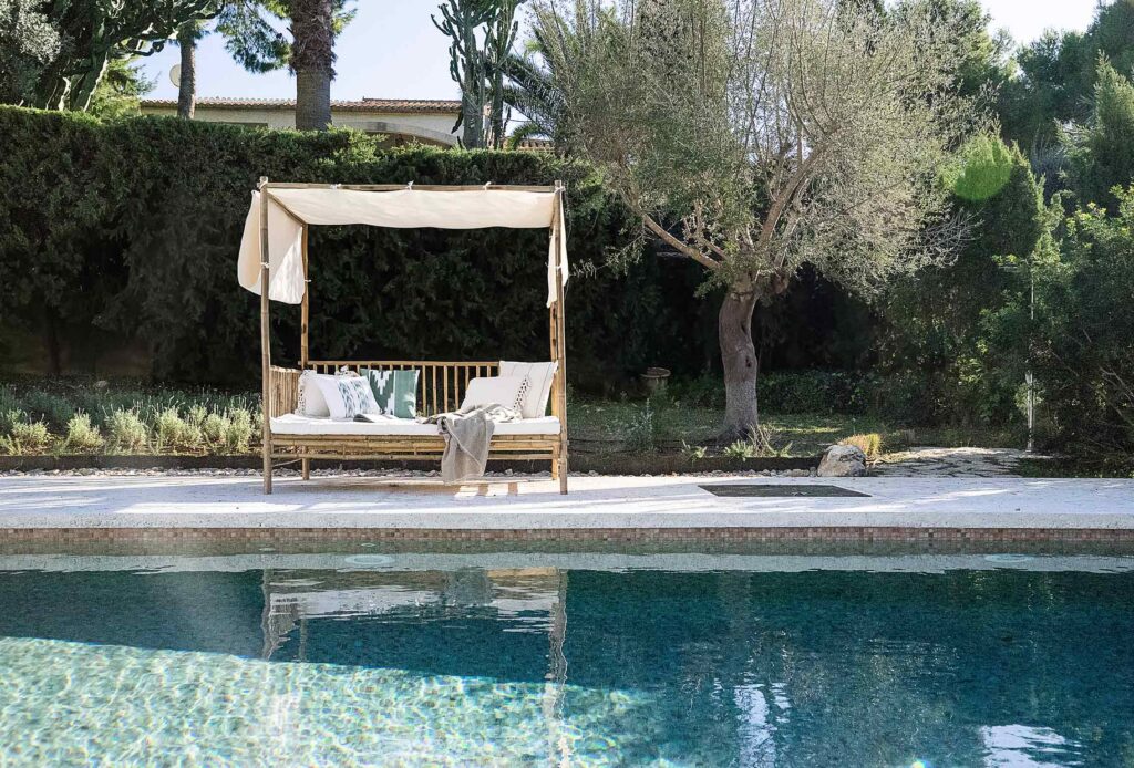 Bambus-Daybed mit weißem Stoffbaldachin neben dem Pool und einem Olivenbaum