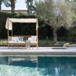 Bambus-Daybed mit weißem Stoffbaldachin neben dem Pool und einem Olivenbaum