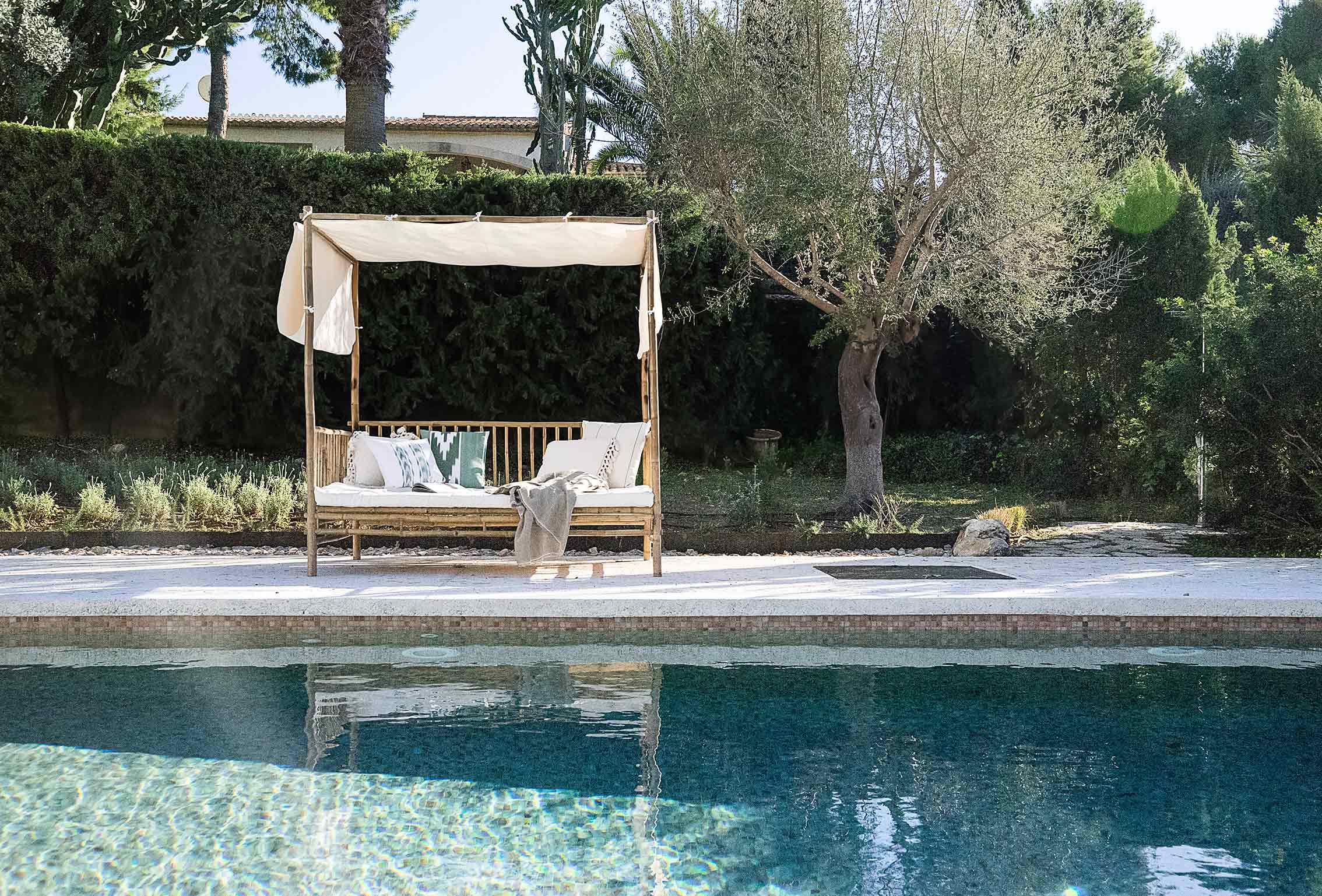 Bambus-Daybed mit weißem Stoffbaldachin neben dem Pool und einem Olivenbaum