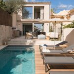 Langgestreckter türkisfarbener Mosaikpool mit Sonnenliegen auf einem Holzdeck vor der Hausfassade