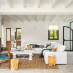 Salón con vigas blancas, sofá blanco, suelo continuo claro y puerta de hierro y cristal en arco