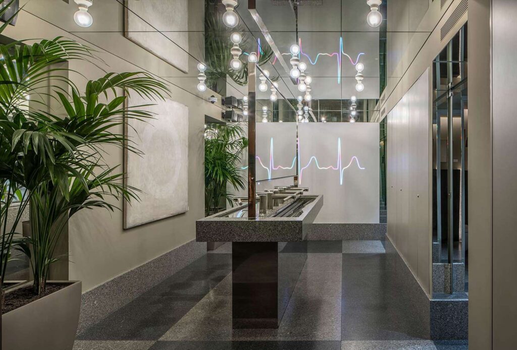 WC with a continuous grey stone basin, light bulbs, mirrors and a heartbeat line of light on the wall