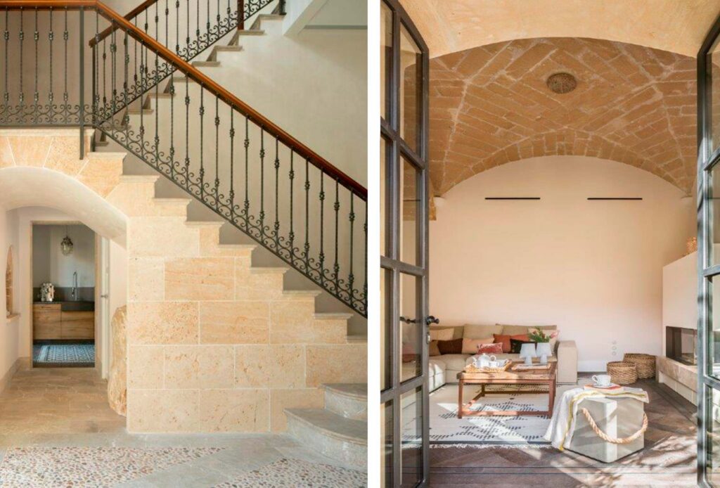 Escalera de piedra con barandilla de forja y salón con bóveda de piedra tras puertas acristaladas