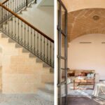 Escalera de piedra con barandilla de forja y salón con bóveda de piedra tras puertas acristaladas