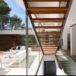 Escalera de peldaños de madera junto a cristalera con vistas a la terraza de sofás blancos