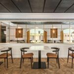 Dining room with white marble tables, dark chairs with cognac seats, a wine cabinet and a mirrored wall
