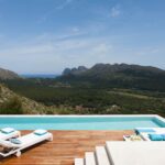 Pool und weiße Sonnenliegen auf einem Holzdeck mit Blick auf Tal, Berge und Meer
