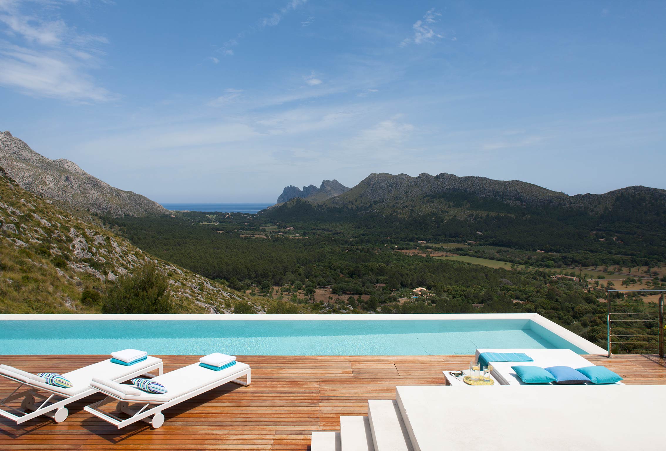 Pool und weiße Sonnenliegen auf einem Holzdeck mit Blick auf Tal, Berge und Meer