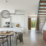 White kitchen with island open to the dining area, timber staircase and light stone floor