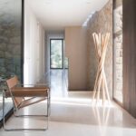 Pasillo con muro de piedra, suelo claro pulido, silla de cuero y perchero de madera