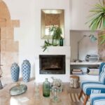 Rincón del salón con chimenea blanca, arco de piedra, sillones de rayas azules y jarrones calados