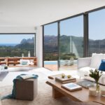 Wohnzimmer mit weißen Sofas, Holztisch und großen Fenstern mit Blick auf Berge und Meer