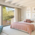 Schlafzimmer mit großem Bett, rosa Tagesdecke, weißen Balken und großem Fenster mit Balkon und Bergblick