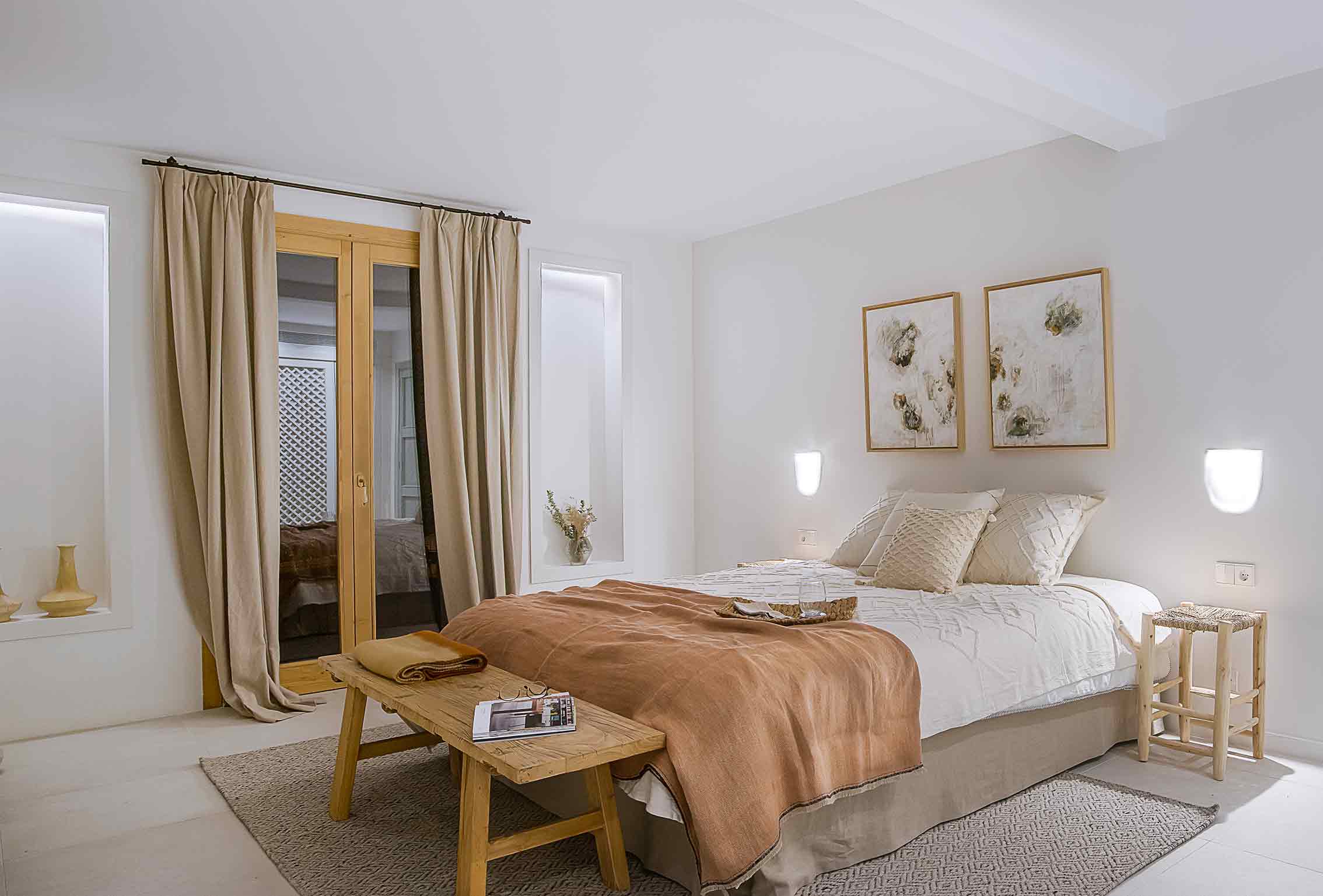 Schlafzimmer mit terrakottafarbener Decke, Holzbank, beigen Vorhängen, zwei Bildern und beleuchteten Nischen
