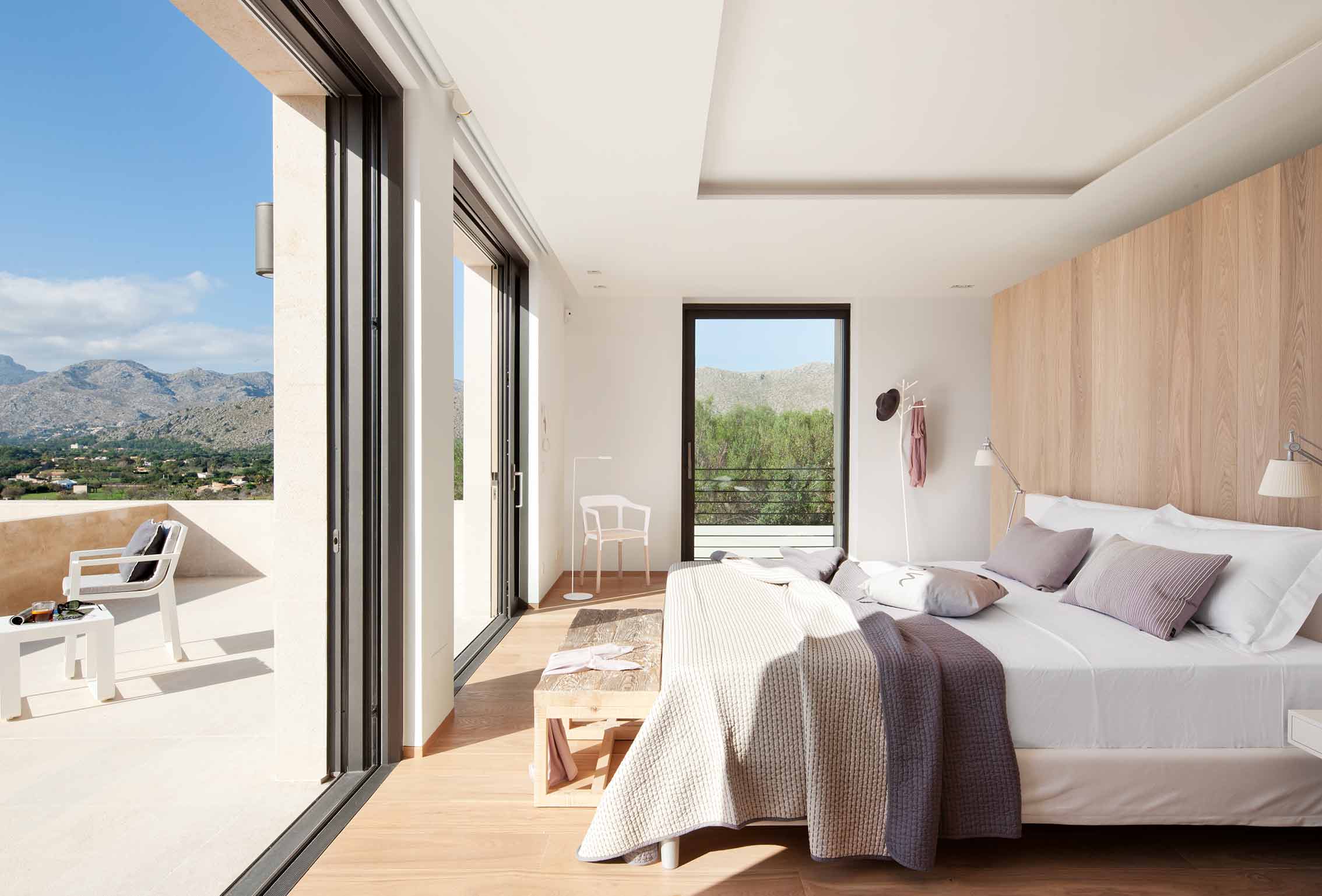 Dormitorio con cabecero de madera clara, suelo de roble, terraza abierta y vistas a la montaña