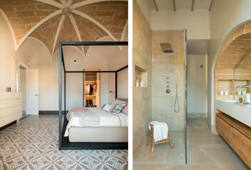 Dormitorio con cama de estructura negra bajo bóveda de piedra y baño con ducha de mármol beige
