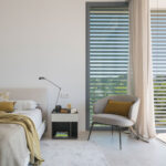 Bedroom with mustard cushions, grey armchair, slatted screen and light curtain beside the terrace