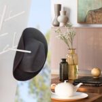 Detalle decorativo con perchero blanco, sombrero y pañuelo, y mesa de madera con jarrones, libros y tetera