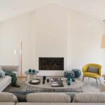 Wohnzimmer mit Einbaukamin, beigem Sofa, gelbem Sessel und blauen Hockern unter dem Satteldach
