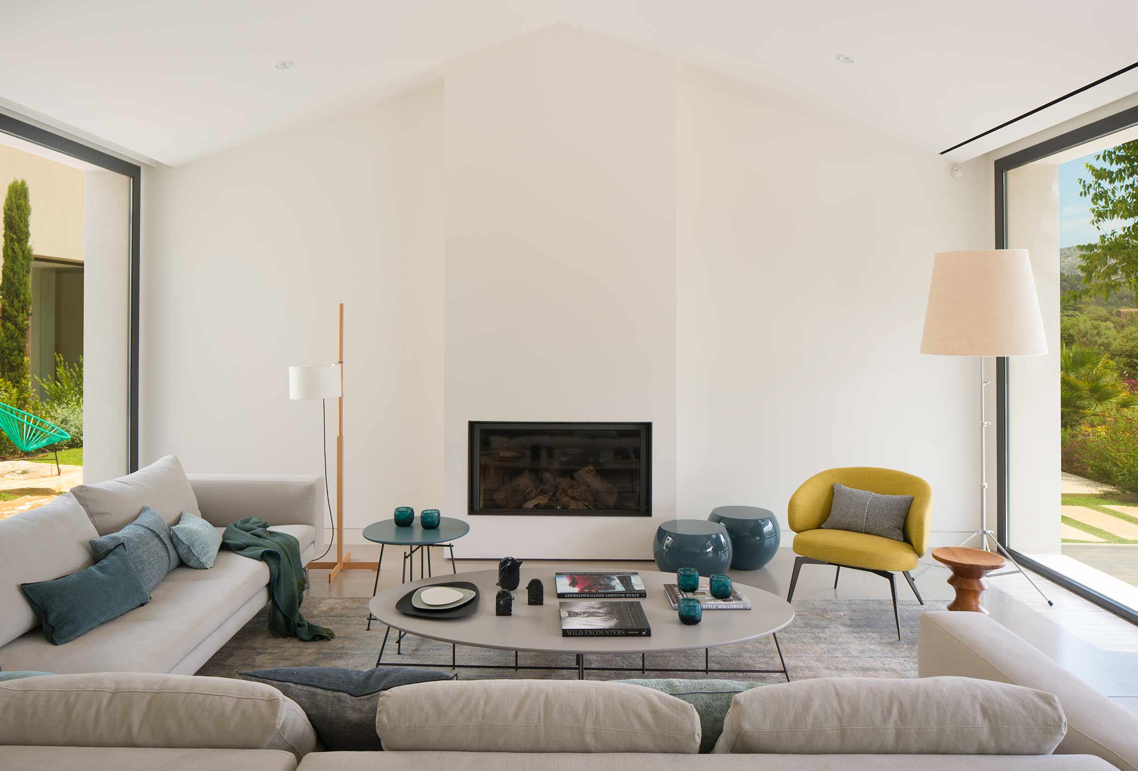 Wohnzimmer mit Einbaukamin, beigem Sofa, gelbem Sessel und blauen Hockern unter dem Satteldach