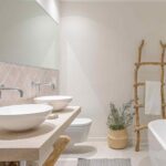 Bad mit diagonal verlegten rosa Fliesen, zwei Waschbecken, freistehender Badewanne und rustikaler Handtuchleiter aus Ästen