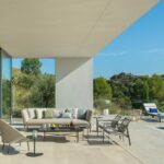 Light stone terrace with sofa, armchairs and sun loungers beside the pool, with hillside beyond