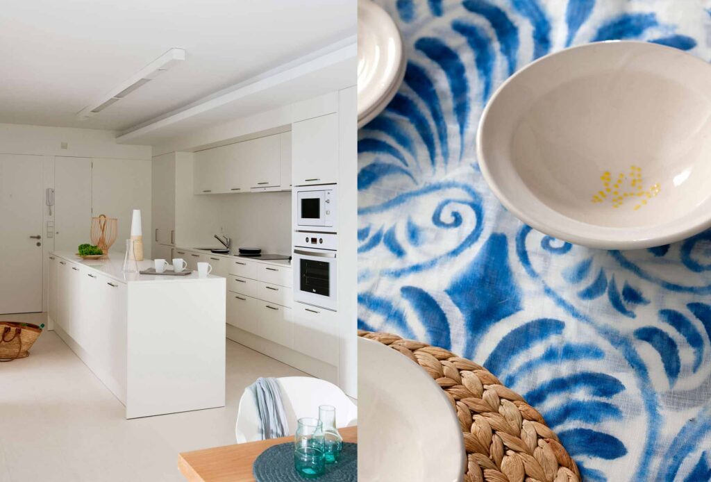 Weiße Küche mit Kochinsel und Einbaugeräten, dazu Detail einer blauen Tischdecke mit Keramikschalen