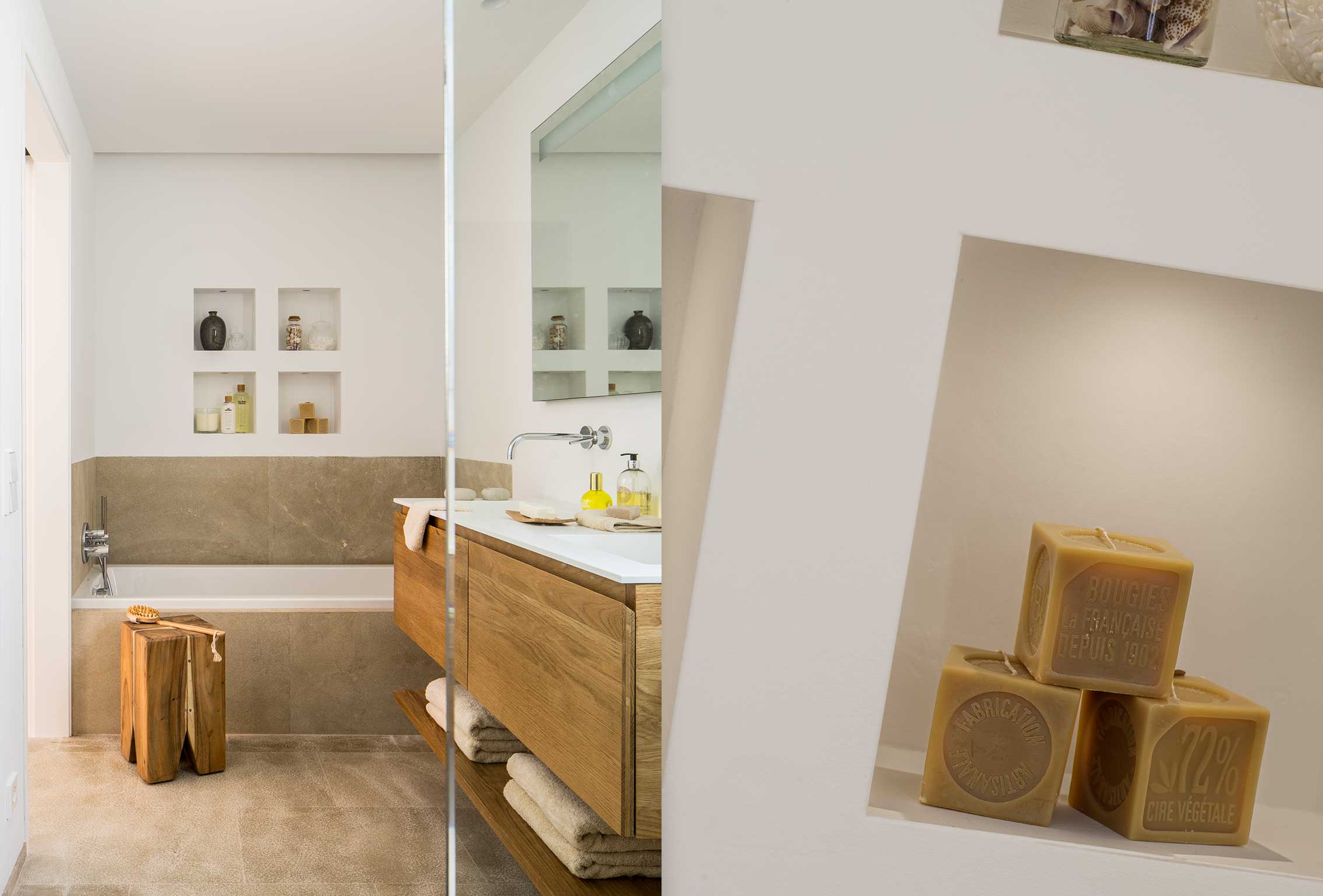 Baño con mueble de madera, bañera y piedra beige, junto al detalle de unos jabones en una hornacina