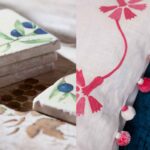 Detalles decorativos: losetas apiladas con olivo pintado y cojín blanco con pompones rosas sobre terciopelo azul