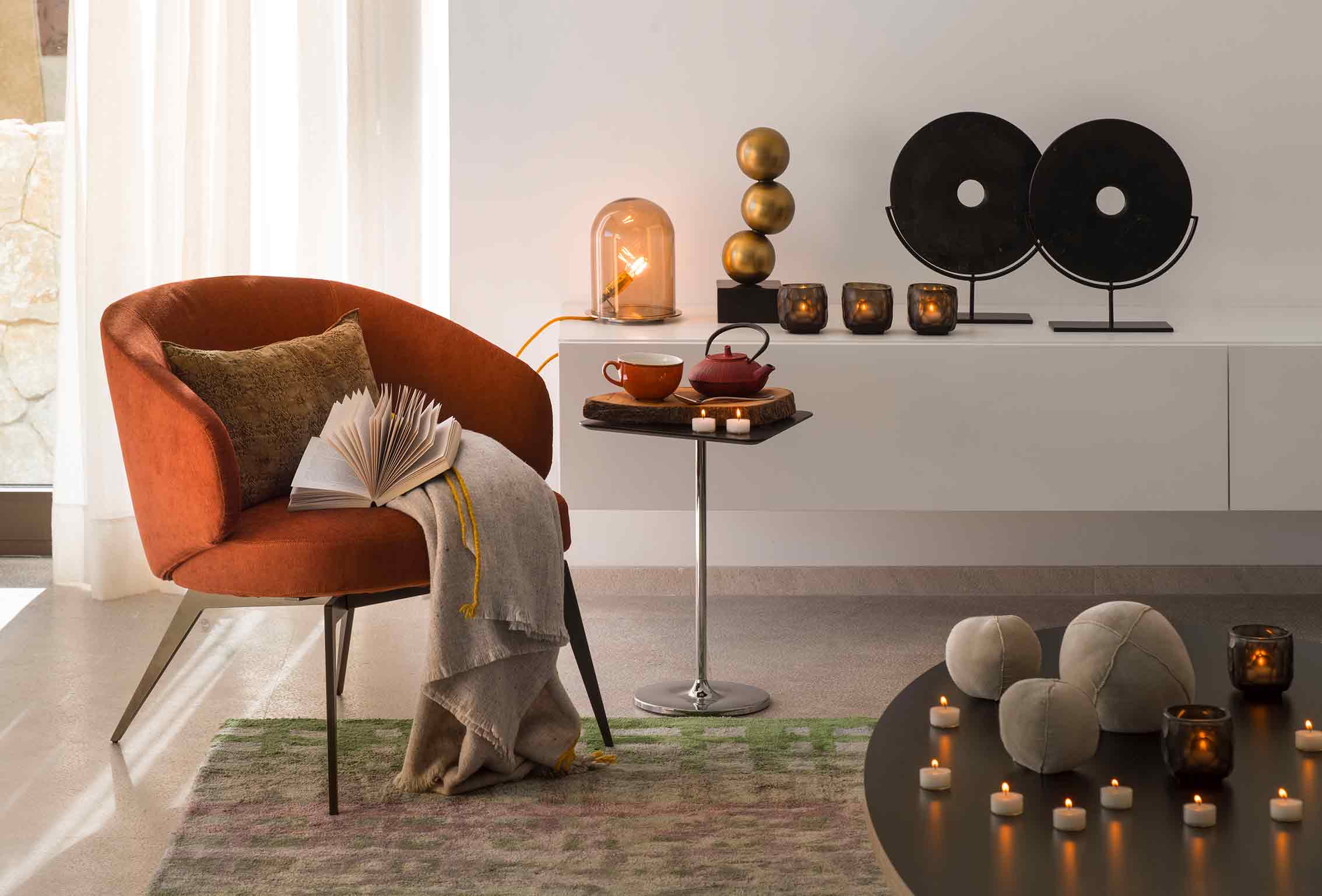 Detalle de butaca naranja con manta y libro, mesita con tetera, velas y discos decorativos negros