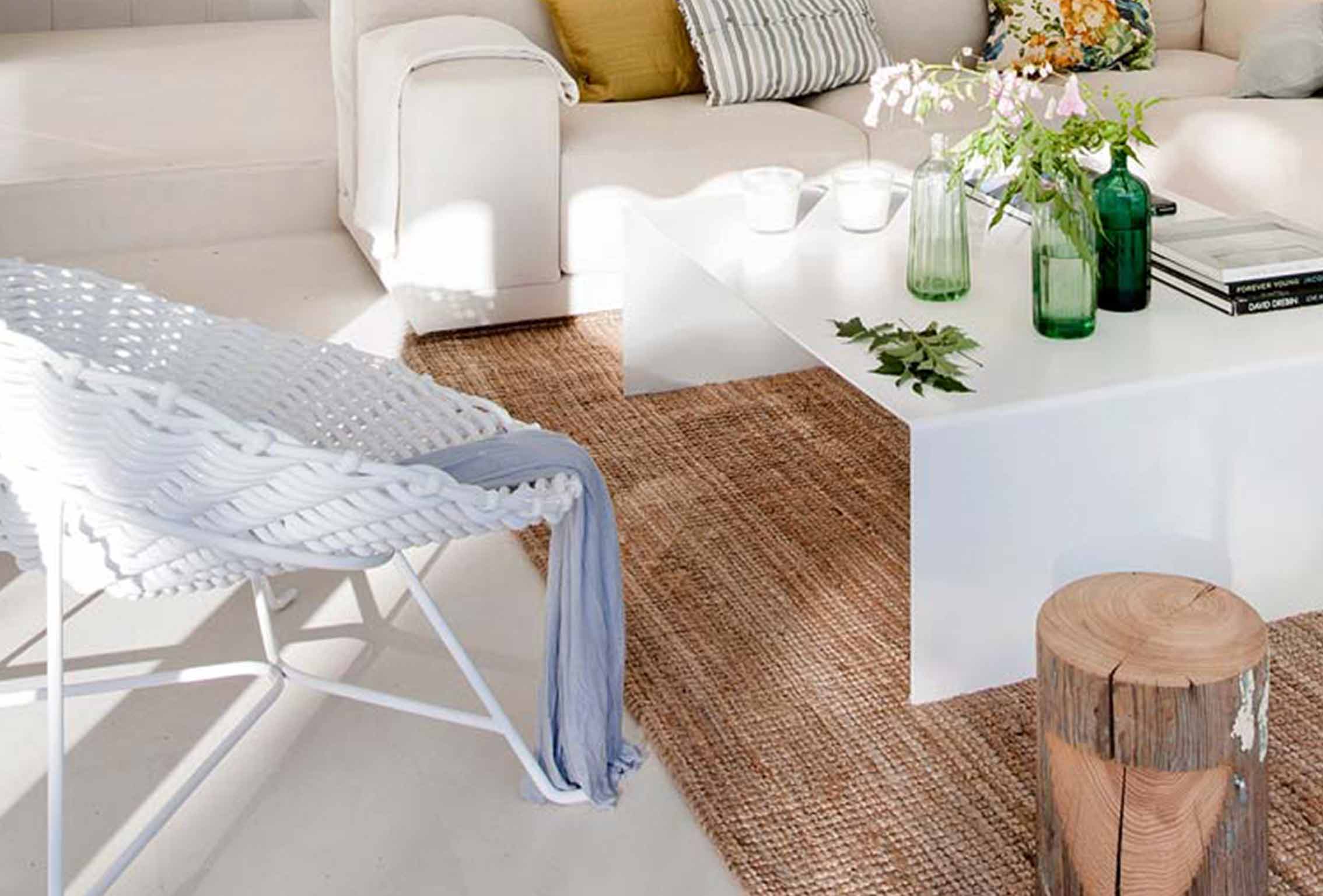 Detail mit weißem Seilsessel, grünen Flaschen auf weißem Tisch, Jutteppich und Baumstammhocker
