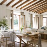 Mesa de comedor con mantel gris, sillas de madera y cuerda, lámparas colgantes y sofá al fondo