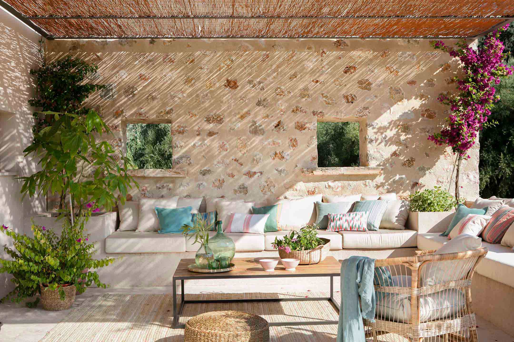 Veranda mit gemauerter Sitzbank, türkisfarbenen Kissen, Schilfgitter und Bougainvillea neben einer Steinmauer