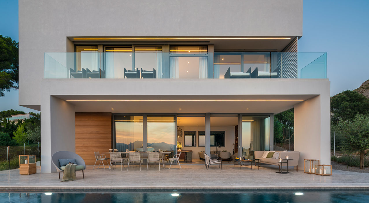 Fachada de Alfabaguera al anochecer con terraza iluminada, piscina y balcón de cristal