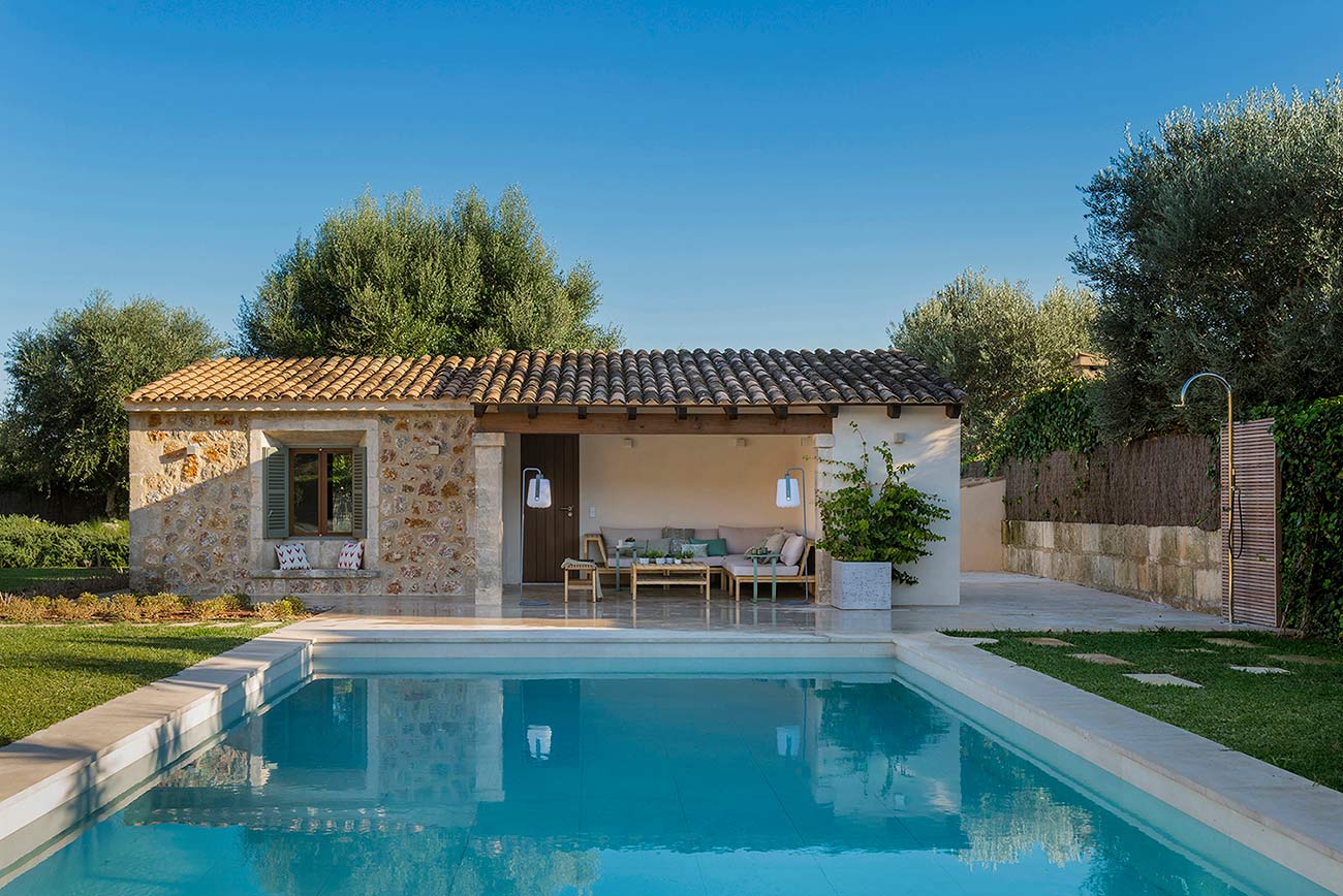 Small stone house with a porch and seating area beside the swimming pool surrounded by olive trees