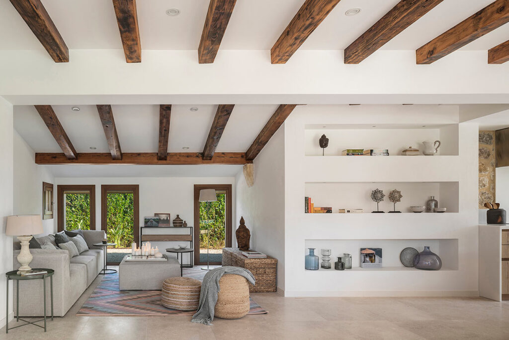 Salón con vigas de madera vistas, sofá gris, estanterías blancas empotradas y suelo beige