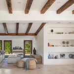 Salón con vigas de madera vistas, sofá gris, estanterías blancas empotradas y suelo beige