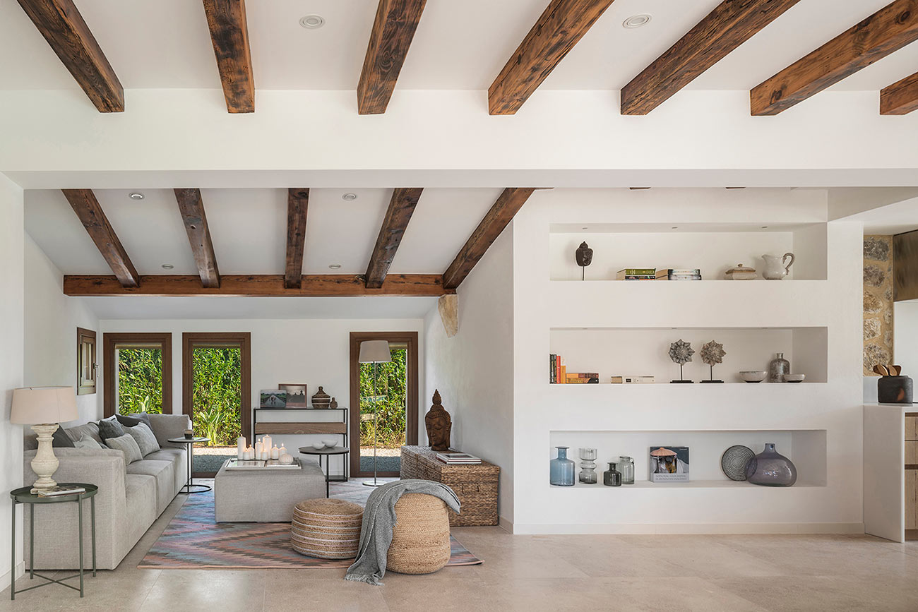 Salón con vigas de madera vistas, sofá gris, estanterías blancas empotradas y suelo beige